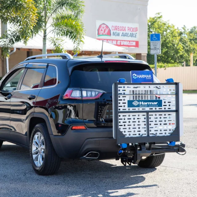 Black SUV parked in a lot with a Hamar lift attached to the rear, near a store with a visible curbside pickup sign.